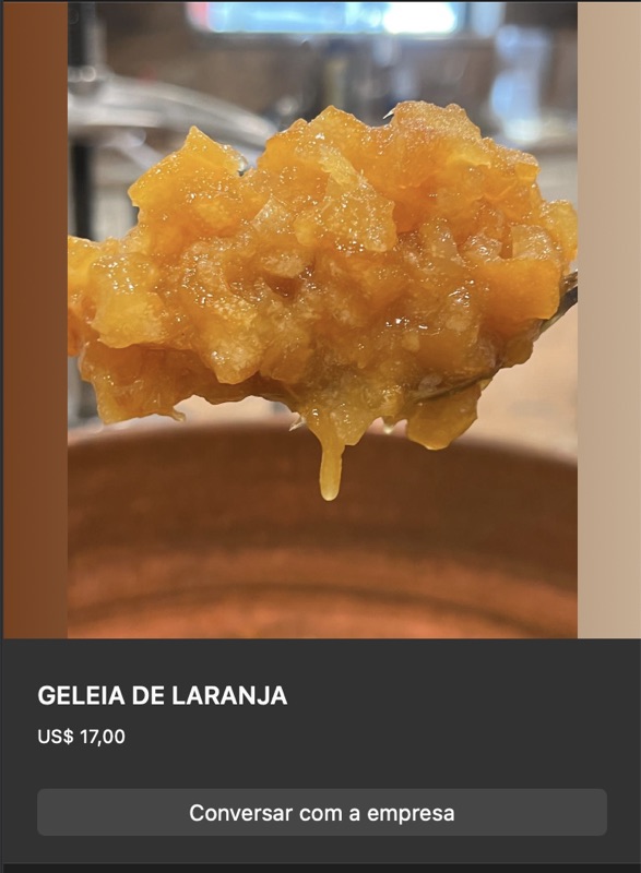 Colher cheia de geleia de laranja com pedaços de casca, cor laranja-dourada, textura brilhante e espessa. Pote de vidro ao fundo.