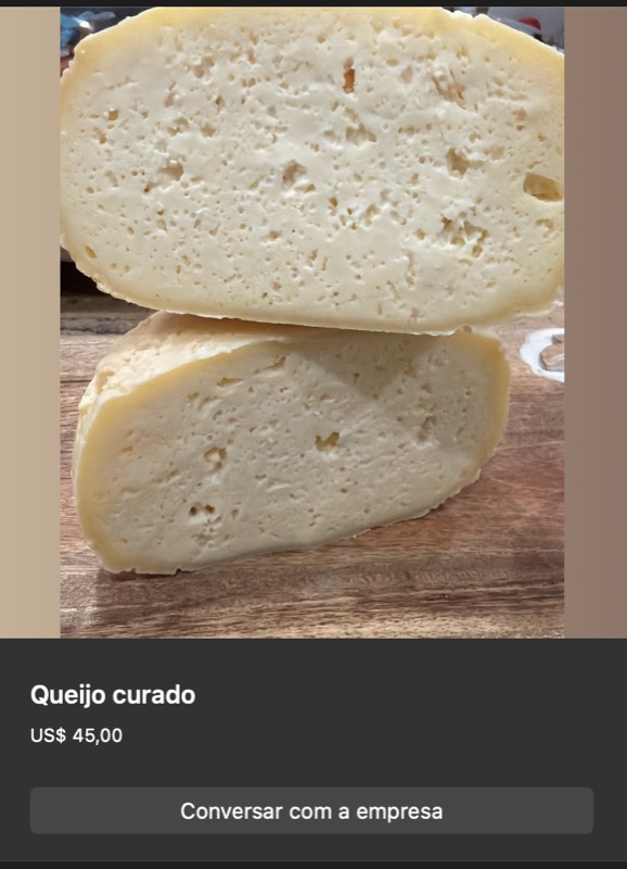 Queijo curado em formato arredondado, cor amarelo-creme pálido, partido ao meio mostrando textura interna firme com pequenos olhos. Sobre tábua de madeira.