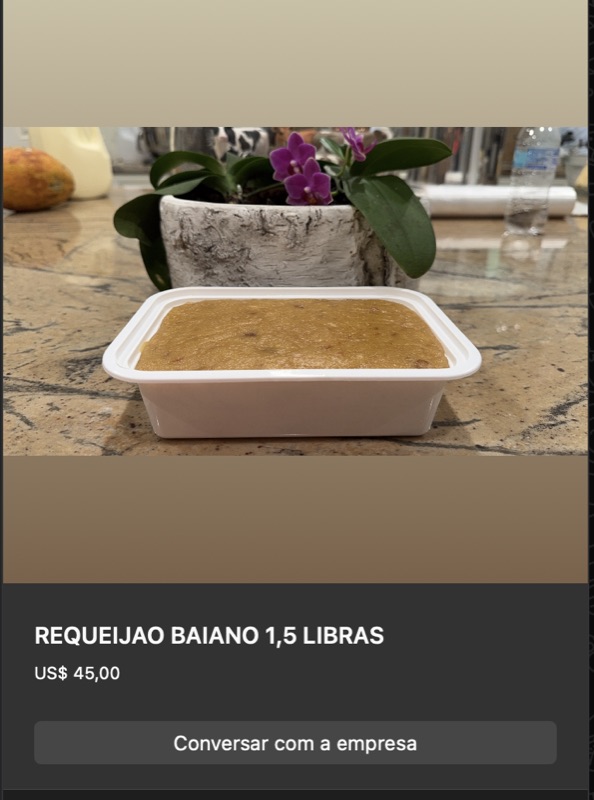 Recipiente quadrado plástico transparente com requeijão baiano em bloco cor amarelo-dourada, superfície ligeiramente irregular. Sobre balcão de granito com orquídea branca ao fundo.