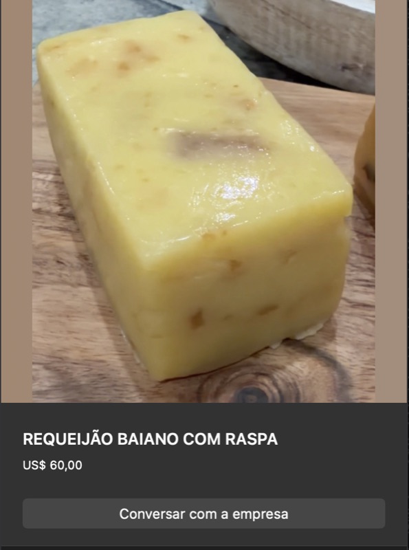 Bloco retangular de requeijão baiano cor amarelo-dourada com pequenas manchas escuras (raspa caramelizada) visíveis na superfície. Sobre tábua de madeira clara.
